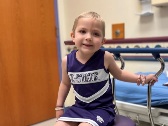 A young girl with short hair in a K-State cheerleading outfit at a clinic.