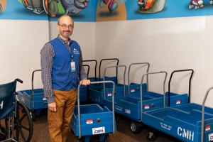 Terrence Gallagher at Children's Mercy Hospital. He is wearing his blue volunteer vest and standing next to a hospital wagon.