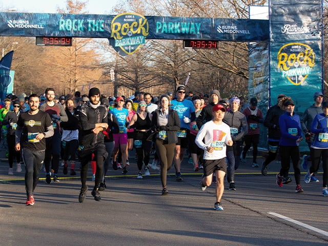 A group of runners runs under a Rock the Parkway banner