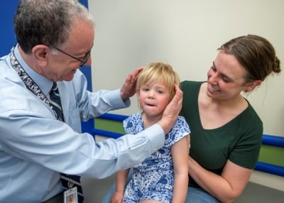 A clinician exams a young girl head while she sits in a caregiver's lap.