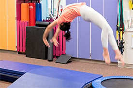 Gabby using a trampoline to do a back handspring in a gym setting.