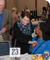 2024 Scholarship Award Celebration donor chatting with a scholarship recipient who is sitting at table 23 at the celebration breakfast.