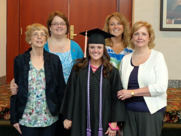 A woman in a graduation gown in surrounded by female family members