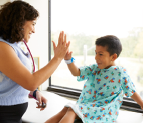 A Children's Mercy provider smiling and giving a patient in a hospital gown a high-five.