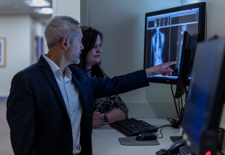 A man and a woman look at a monitor of x-rays showing a spine.