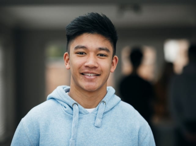 An Asian teen boy in a gray hoodie in front of a blurred background