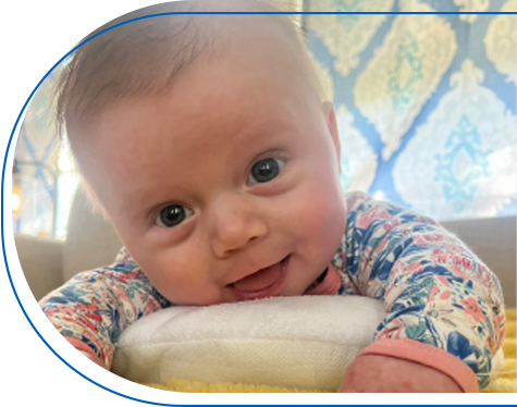 Baby Brexley laying on her stomach and smilng while looking into the camera.