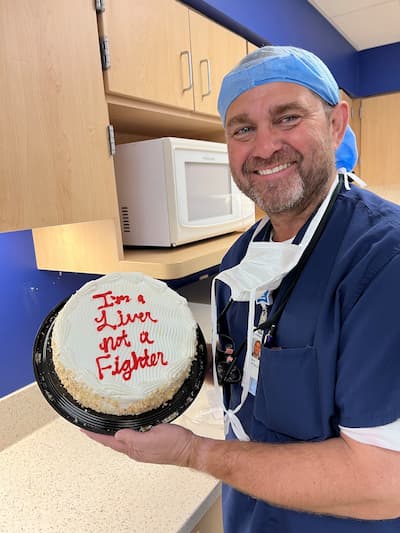 Dr. holds cake in celebration of 100th liver transplant.