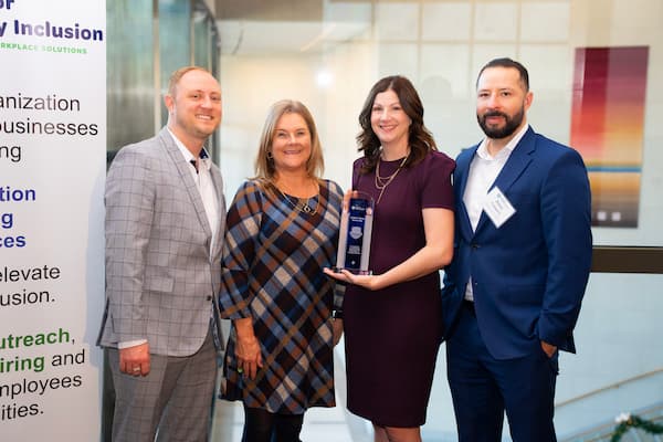 Four people in business wear stand together, smiling and holding a trophy that features the Center for Disability Inclusion logo and reads: “Children’s Mercy Kansas City: In recognition of outstanding achievement for 2024 Leader in Disability Inclusion.”  