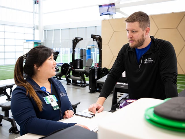 Two Sports Medicine fellow talking to each other with weight equipment in background