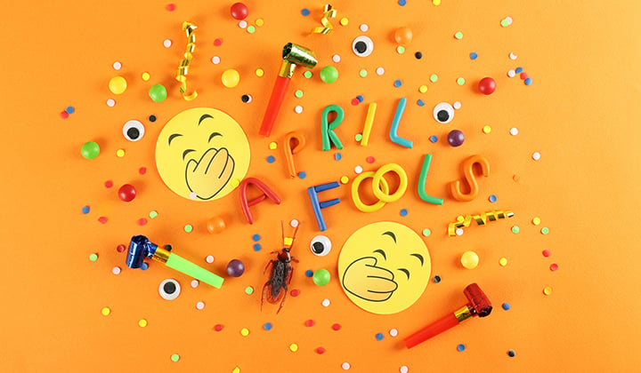 Confetti, laughing emojis, party horns and a fake bug spread out on a table with April Fools text.