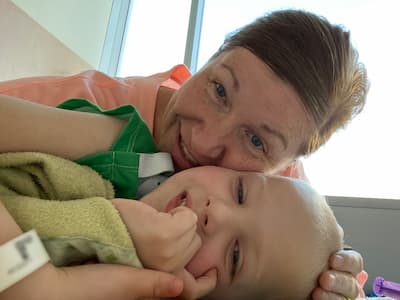 A close-up photo of a Mom and little boy snuggling. The little boy is wearing a hospital gown and bracelet.