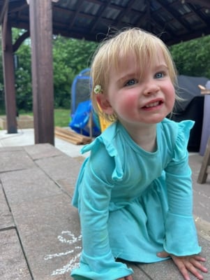 Toddler girl June wears a swimsuit and hat as she plays by a picnic table in a wading pool.