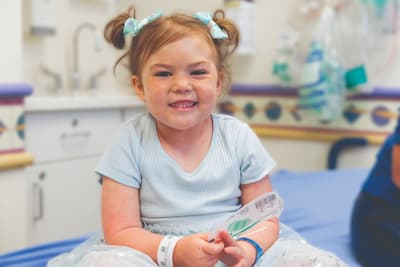 Mayia sitting, wearing light blue dress smiling with two bows in hair