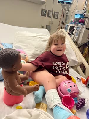 Zaylee wearing burgundy t-shirt playing with toys in hospital bed